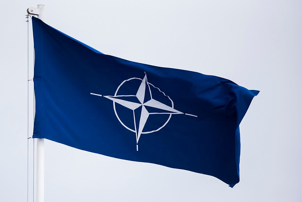 Flaga NATO powiewająca podczas uroczystości wojskowej.